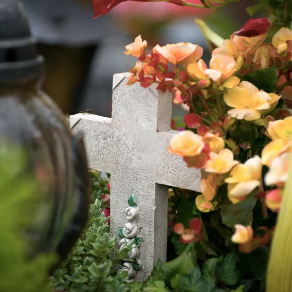 Steinernes Grabkreuz auf einem Friedhof, umgeben von Blumen und Grabschmuck – ruhige, würdige Atmosphäre als Symbol für Erinnerung, Abschied und letzte Ruhestätte auf dem Friedhof Bochum-Werne.