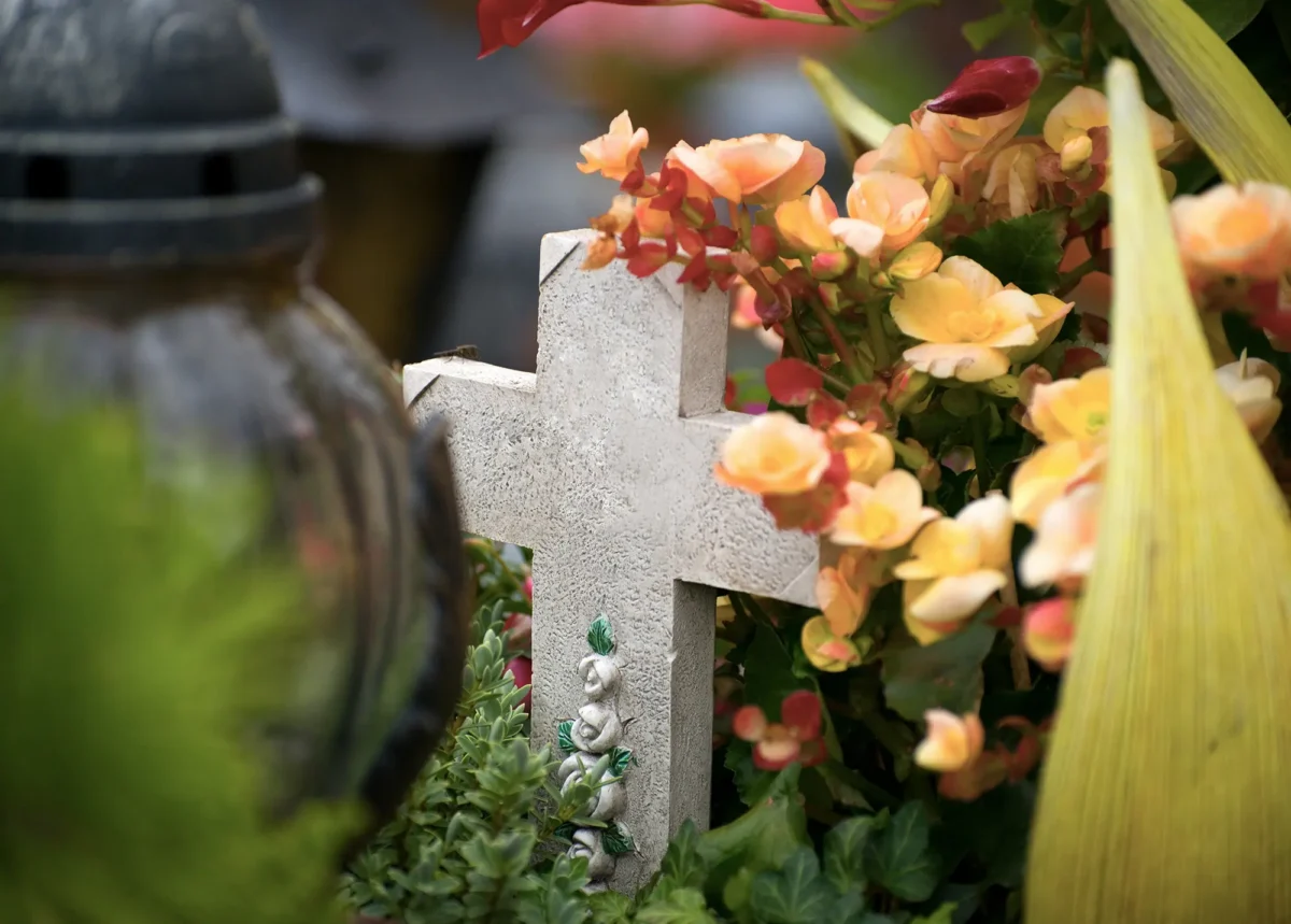Steinernes Grabkreuz auf einem Friedhof, umgeben von Blumen und Grabschmuck – ruhige, würdige Atmosphäre als Symbol für Erinnerung, Abschied und letzte Ruhestätte auf dem Friedhof Bochum-Werne.