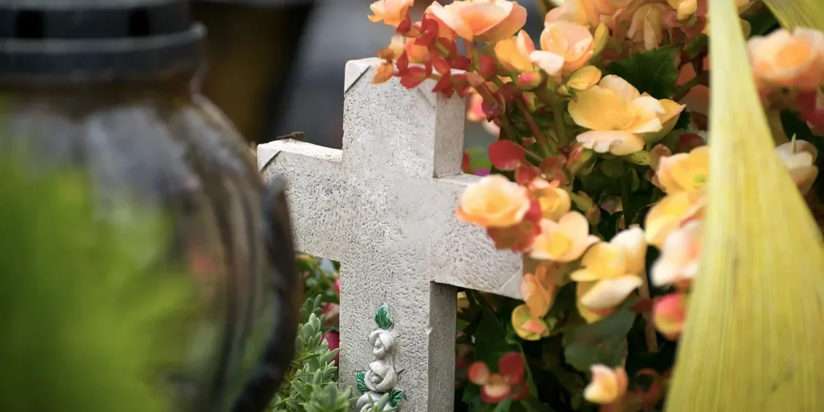 Steinernes Grabkreuz auf einem Friedhof, umgeben von Blumen und Grabschmuck – ruhige, würdige Atmosphäre als Symbol für Erinnerung, Abschied und letzte Ruhestätte auf dem Friedhof Bochum-Werne.